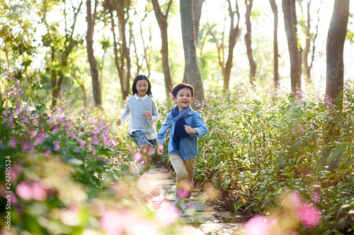 two little asian kids running in flower field in woods