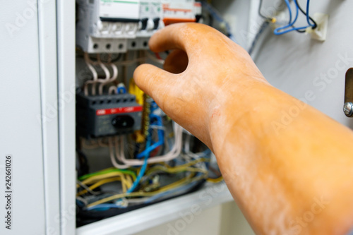 the hand of a man in a dielectric glove with a screwdriver moves towards the switchboard