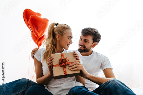 Couple. Love. Valentine's day. Woman is holding a gift box and looking at her man, both are smiling