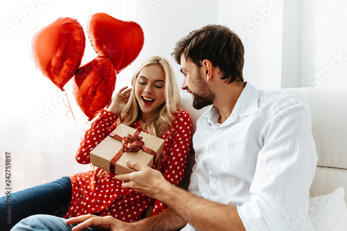 Couple. Love. Valentine's day. Emotions. Man is giving a gift box to his woman, both smiling; at home