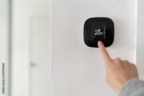 Smart home digital thermostat touch screen woman touching touchscreen to adjust temperature of heating in living room wall.