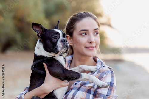 Young girl holding on hands her boston terrier black and white dog on the beach