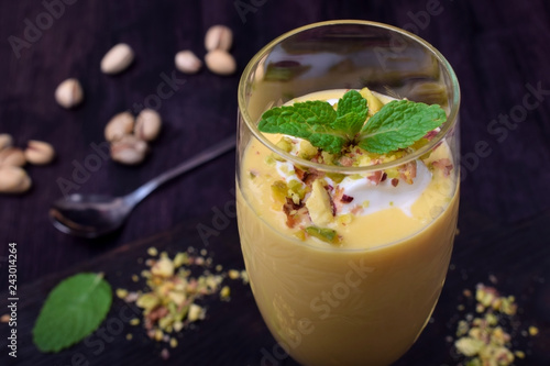 Mango yogurt dessert in a champagne glass topped with pistachios and mint against the dark background