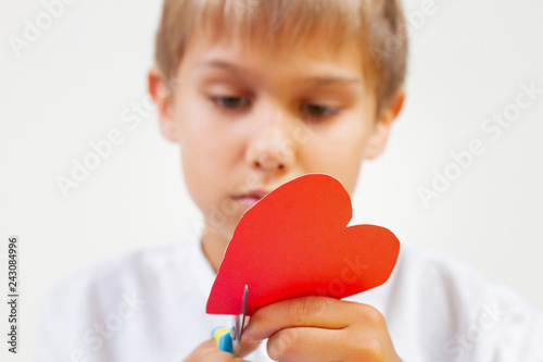 Red paper heart in kid hands. Child cutting red paper heart with scissors