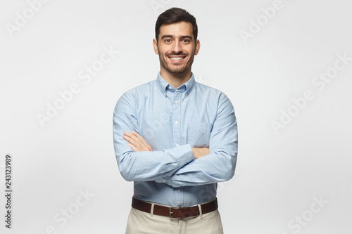 Modern business man in casual blue shirt standing with crossed arms, isolated on gray background