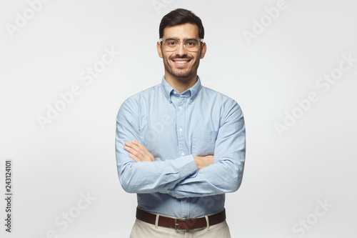 Modern businessman in blue shirt standing with crossed arms, isolated on gray background