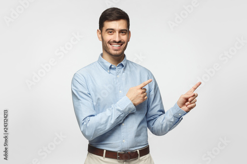 Happy smiling young business man pointing away, isolated on gray background