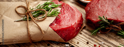 two pieces of meat from the butcher shop, one piece of meat wrapped in paper. A piece of beef in the form of a steak on a wooden background with ingredients