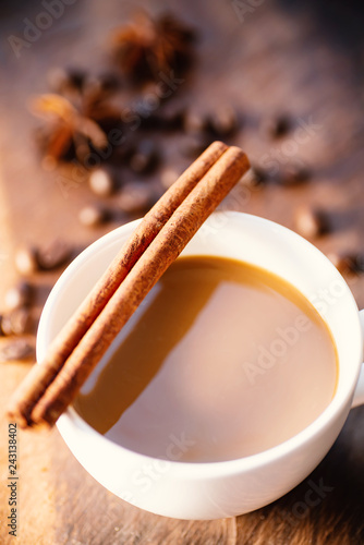 Cup of coffee with cinnamon stick, star anise and roasted coffee beans on wooden table, hot drink