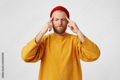 The guy holds fingers on temples, his eyes are squinting, trying to remember something. Bearded man feels headache, massages his temples with fingers, isolated on a white background.