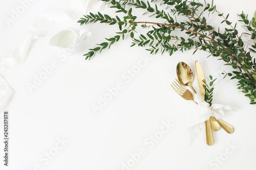 Festive wedding, birthday table setting with golden cutlery, eucalyptus parvifolia, silk ribbon and milk pitcher on white table background. Rustic restaurant menu concept. Flat lay, top view. Empty