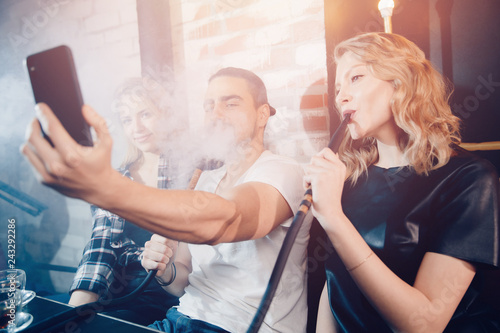 Smoke hookah shisha in bar and nightclub, team of friends take selfie photos on phone