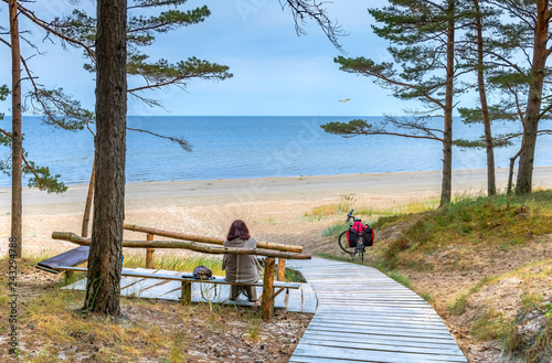 Happy woman is resting on wooden bench and looking at the distance on sandy beach of the Baltic Sea 