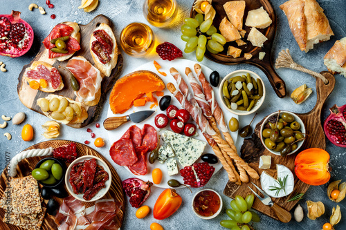 Appetizers table with antipasti snacks and wine in glasses. Brushetta or authentic traditional spanish tapas set, cheese and meat platter over grey concrete background. Top view