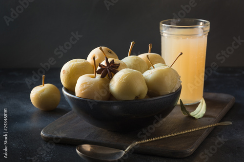 Pickled apples in bowl and apple sidr on dark stone table.