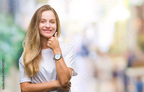 Young beautiful blonde woman wearing casual white t-shirt over isolated background looking confident at the camera with smile with crossed arms and hand raised on chin. Thinking positive.