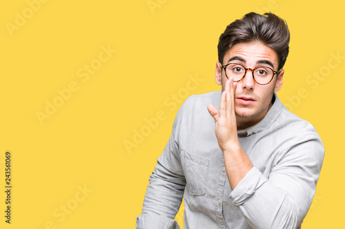 Young handsome man wearing glasses over isolated background hand on mouth telling secret rumor, whispering malicious talk conversation