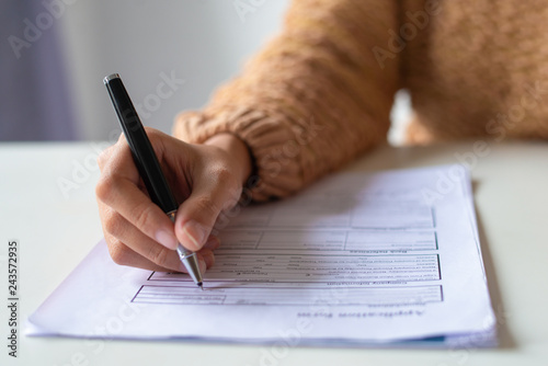 Close-up of lady filling application form. Unrecognizable woman in sweater sitting at table and preparing her resume. Job search concept