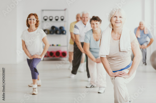 Smiling senior woman exercising with group of active seniors in fitness center