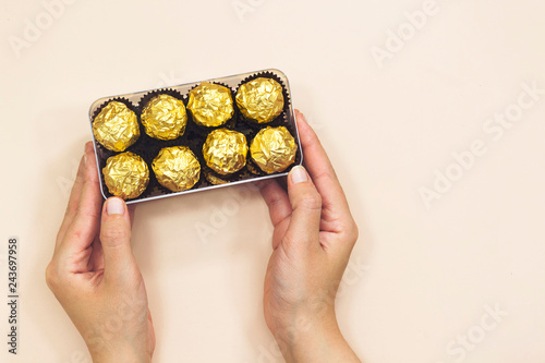 closeup hand woman holding a box of golden premium chocolate sweets for valentine's or women's holiday