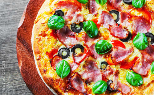 Pizza with Mozzarella cheese, ham, pepper, olive, meat, Tomato sauce, Spices and Fresh Basil. Italian pizza on wooden background
