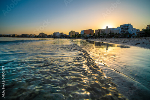 Golden waves of the sea and city on horizon during sunset