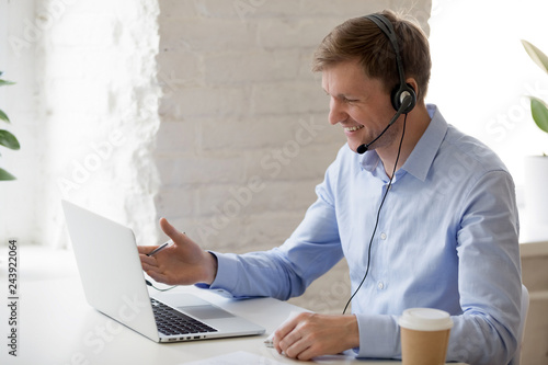 Smiling businessman in headphones looking at laptop screen, watching good webinar, consulting client, distance learning languages, making notes, happy man participating online conference