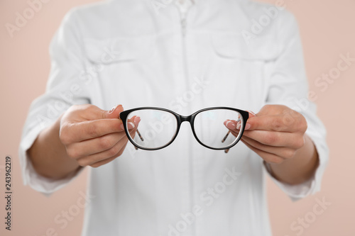 Female ophthalmologist with eyeglasses on light background, closeup