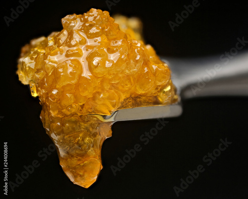 Cannabis concentrate sugar wax dripping off dabbing tool on black background