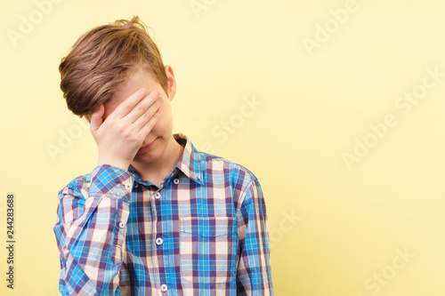 facepalm. shame and embarrassment concept. confused boy covering his face over yellow background, advertisement, banner or poster template, emotion facial expression, people reaction