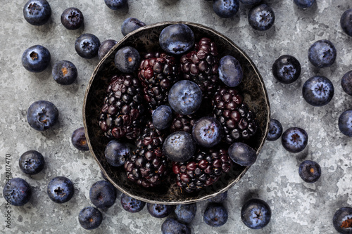 Berries (blueberry,blackberry) in a black bowl. Gray stone background. Top view.