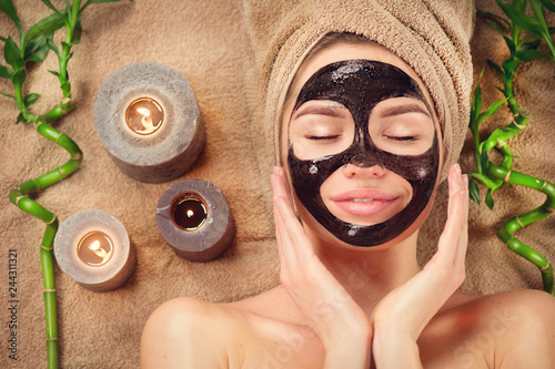 Beautiful woman with black purifying black mask on her face. Beauty model girl with black facial peel-off mask lying in spa salon. Skincare, cleansing