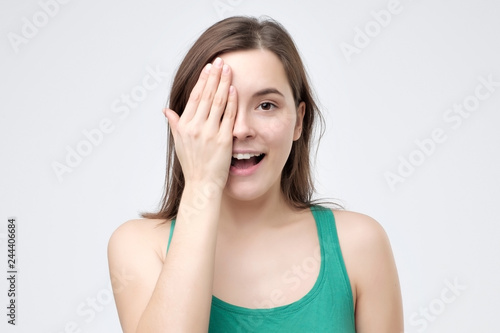 Smiling woman covering an eye with her hand as she stands looking at the camera
