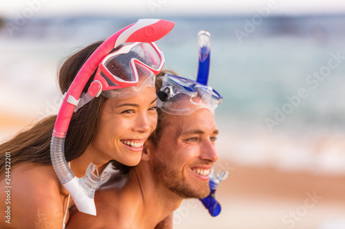 Beach travel people having fun snorkeling. Happy young interracial couple on beach with snorkel mask looking at copy space after swimming on summer vacation. Asian woman, Caucasian man.