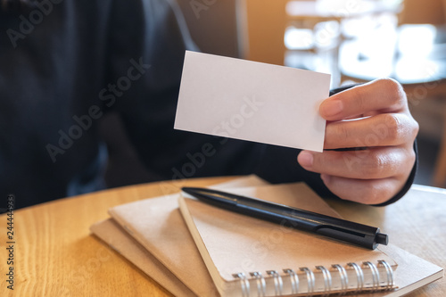 A woman holding and showing a blank empty business card to someone with notebooks on wooden table