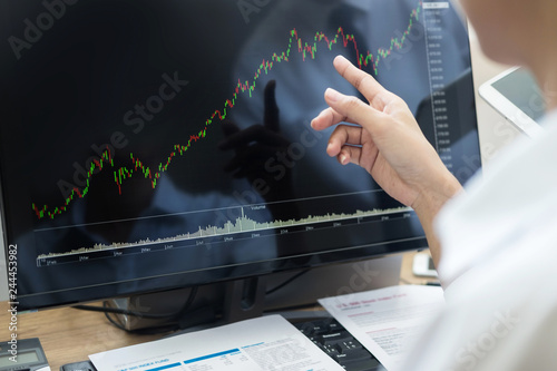 Stock exchange trader Analyzing Graphs chart or data On Multiple Screens in office.