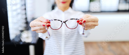 Woman at optician holding eyeglasses she want to buy. Selective focus on glasses.