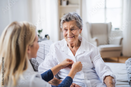 A health visitor helping a sick senior woman sitting on bed at home.