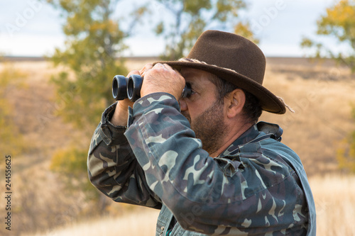 A hunter in a hat with binoculars looks out for prey