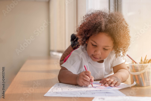 Little toddler girl laying down concentrate on drawing. Mix African girl learn and play in the pre-school class. Children enjoy hand writing. 3 years girl enjoy playing at nursery.