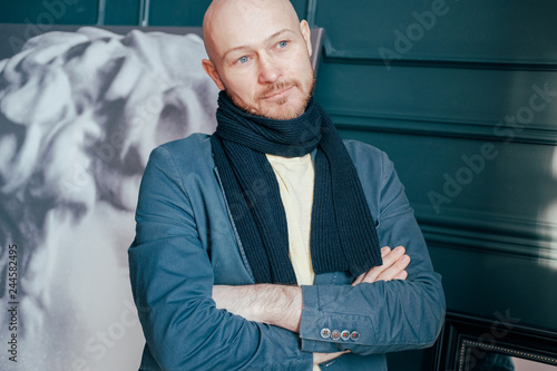 Portrait of attractive adult successful bald man art critic historian with beard in scarf in art gallery