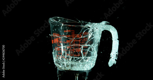 A Glass Measuring Cup Shattering, breaking, exploding into shards isolated on black. Moment of impact