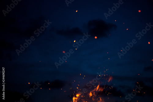Large burning bonfire with soft glowing flame throws flying sparkles all around. Romantic summer evening, people relaxing and enjoying calmness at the seaside during the Night of ancient lights 