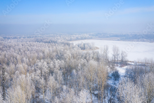 Rime and hoarfrost covering trees. Aerial view of the snow-covered forest and lake from above. Winter scenery. Landscape photo captured with drone.
