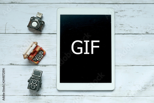 Top view of toys camera,typewriter and tablet written with GIF on white wooden background.