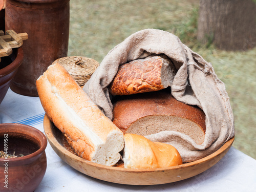 Wooden plate with different kinds of bread. Homespun napkin and tablecloth. Vintage dinnerware and old fashioned household items on historical festival Times and Epochs. Moscow, Russia.