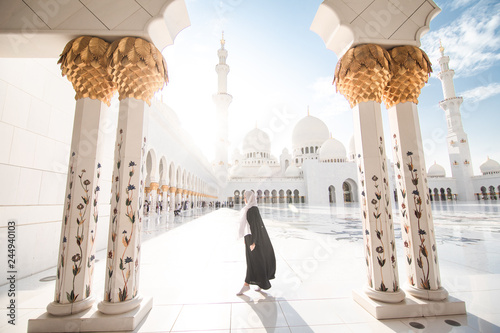 Traditionally dressed arabic woman standing on sun shine wearing black burka visiting Sheikh Zayed Grand Mosque in Abu Dhabi, United Arab Emirates.