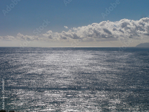 Bright sunlight, blue sky and clouds reflected in the Pacific Ocean of southern California, with Santa Catalina Island on the horizon