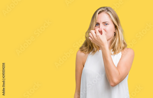 Beautiful young elegant woman over isolated background smelling something stinky and disgusting, intolerable smell, holding breath with fingers on nose. Bad smells concept.