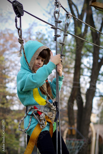 A girl in a hood on a platform for mountaineering on a hanging road. Rope Park